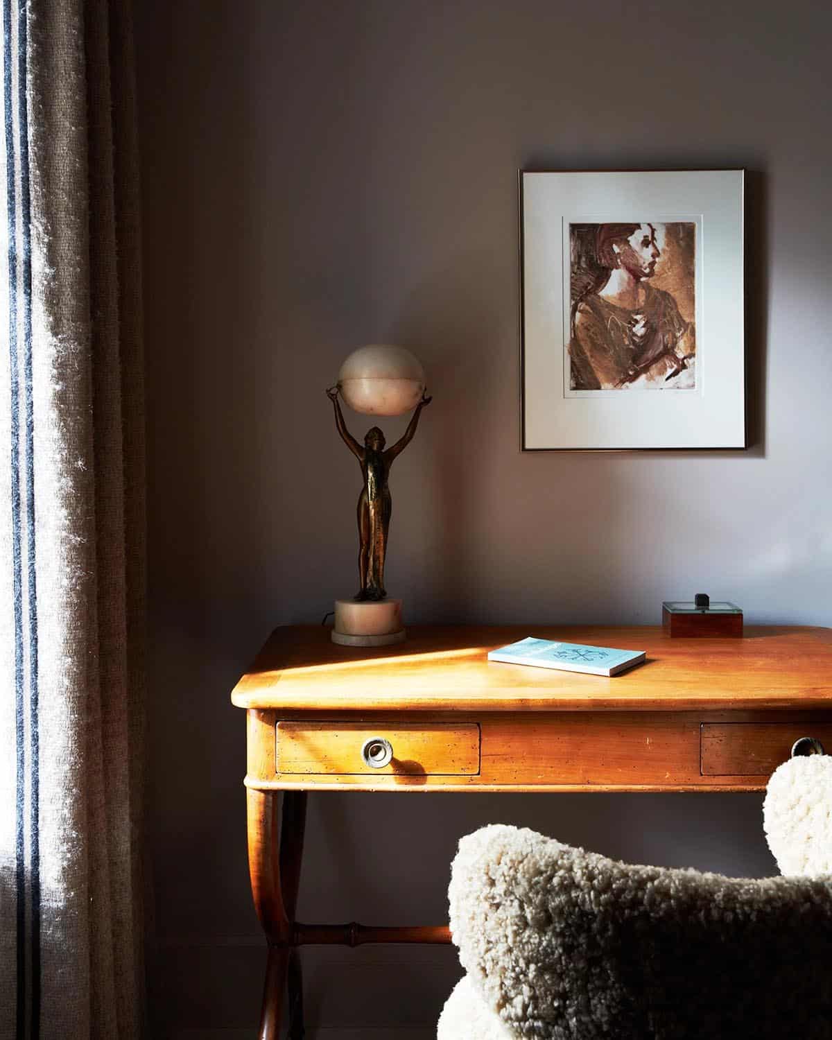 Desk with alabaster figure lamp and framed portrait in window light