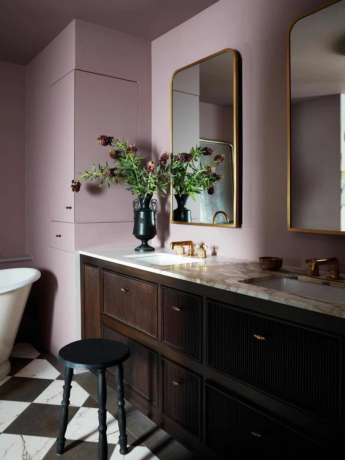 Mauve bathroom with fluted wood vanity, brass mirrors and checkerboard floor