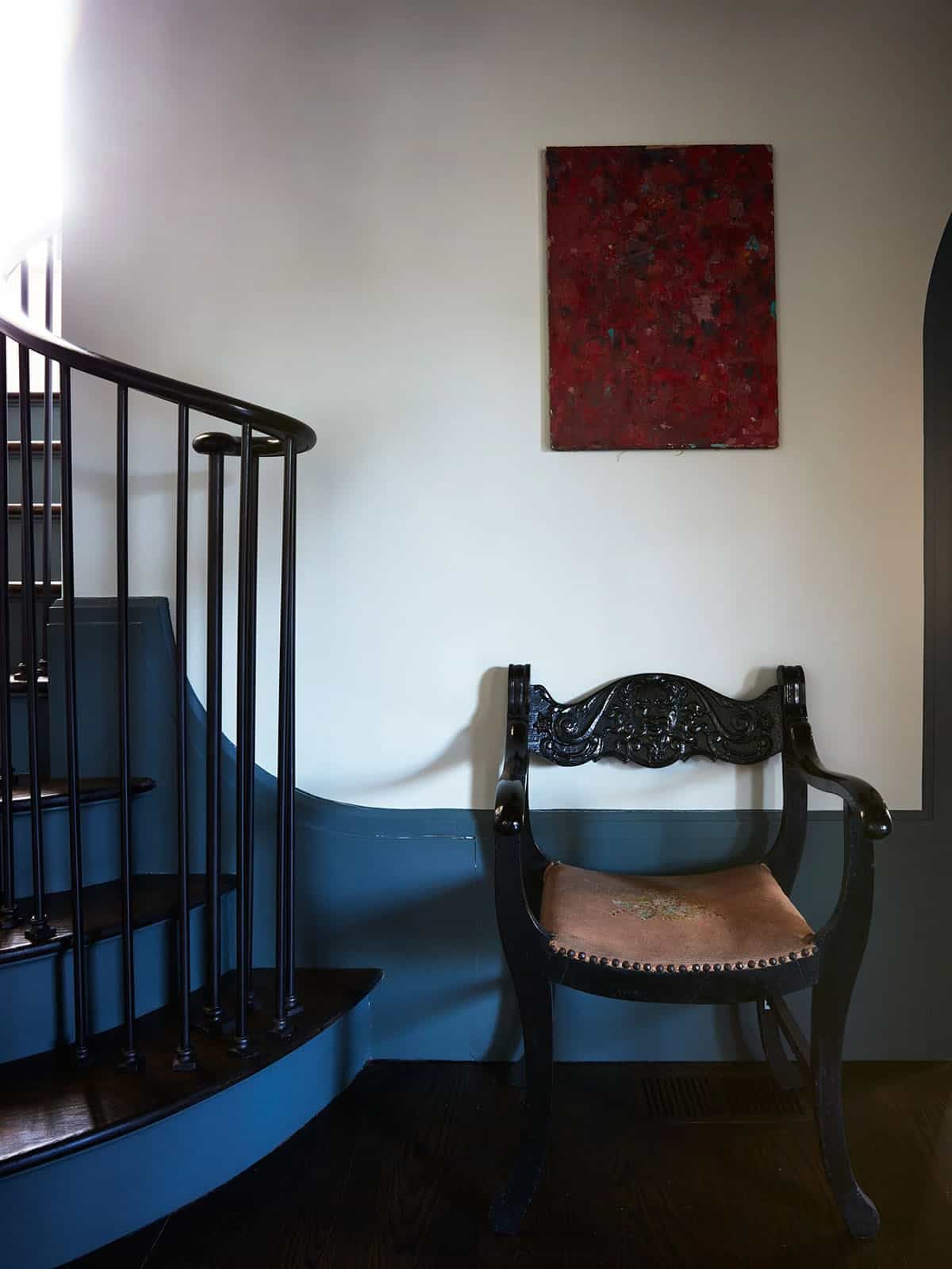 Stair hall with carved antique chair below a red abstract painting